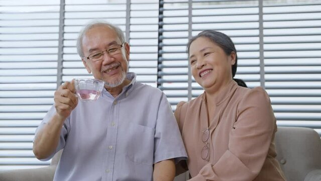 Asian grandfather drinking tea and talking with grandmother in the living room. Senior couple enjoy chatting together at home