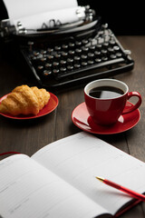 A red cup with coffee. An old vintage typewriter and an empty piece of paper. The notepad and the...