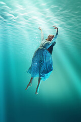 Elegant young woman in delicate dress appears to falling in water, creating dreamlike image....