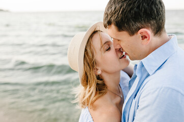 Female kisses male on beach ocean and enjoys sunny summer day. Man embraces woman stands on sand sea. Couple in love hugging and kissing each other on seashore. Spending time together. Closeup face.