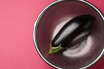 Colander with fresh eggplant on pink table, top view. Space for text