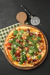 Delicious vegetarian pizza and cutter on black table, top view
