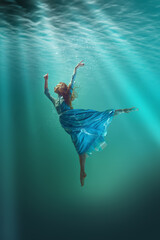 An underwater ballet. Beautiful young girl in elegant dress gracefully levitating underwater with...