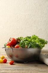 Wet vegetables in colander on wooden table. Space for text