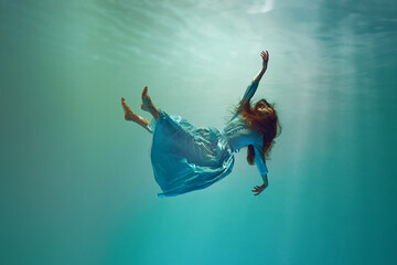 Diving into unknown. Surreal underwater scene featuring elegant young woman levitating gracefully...