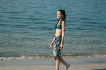 Fototapeta na wymiar young woman with bikini and sarong walking relaxed on the beach