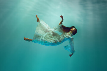 Finding inner peace. Serene underwater moment with elegant young girl in tender white dress...