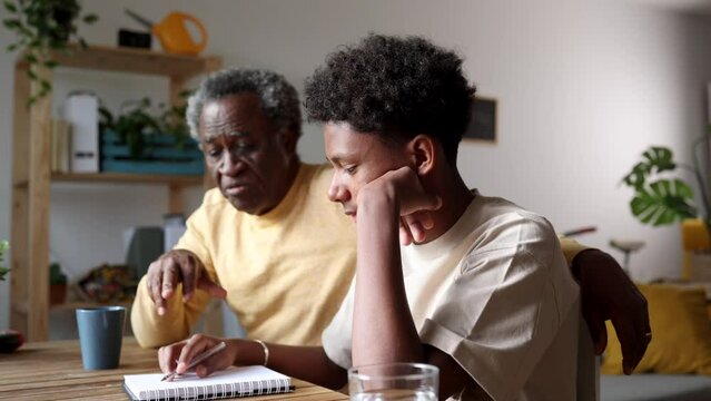 Thoughtful elder explaining schoolwork to his pensive grandson, sharing wisdom at the study table. Grandfather Helping Teenager with Challenging Homework