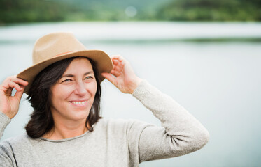 Portrait of beautiful mature woman with hat, standing by lake.
