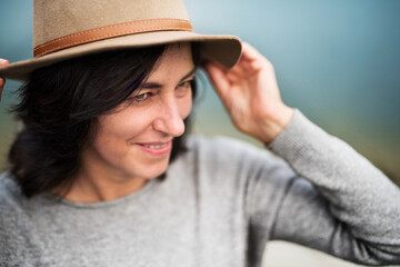 Portrait of beautiful mature woman with hat, standing by lake.