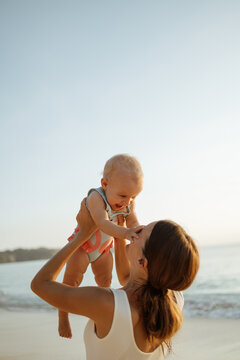 Young mother throws up baby in the sky in front of the sea, summer outdoors. Happy mom and cute smiling baby girl. Positive human emotions, feelings, natural lifestyles. Family background
