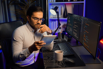 Smart IT developer working on software development coding on pc screen and reading note of newest...