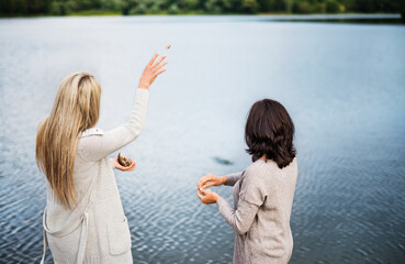 Mom and daughter outdoors, on walk by reservoir, lake embankment, throwing rocks into water....