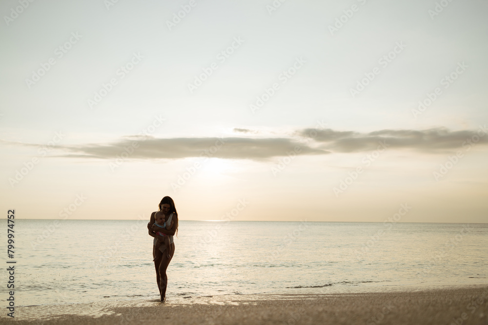 Canvas Prints Mother and baby daughter in swimsuits  playing on the beach at the sunset time. Concept of friendly family.