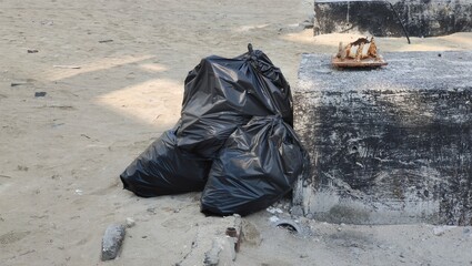 Bunch of tied black plastic garbage disposable bags filled with household junk and waste for recycling and disposal dumped near road or street area for pickup creating environmental pollution.