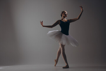 Young ballerina in elegance white tutu and pointe shoes dancing against dark background.