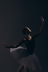 Young ballerina in elegance white tutu dancing against dark background.