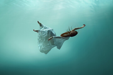 Magic and mystery hidden beneath the ocean. Elegant young girl levitating underwater, finding peace...