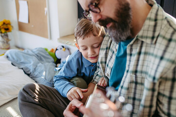 Father teaching boy to play on acoustic guitar. Mesmerized son listening dad making music. Concept...