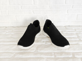 Black cloth sports sneakers on a white brick background
