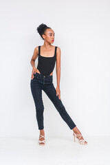 Fashionable young woman in black bodysuit and jeans posing on white background
