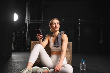 Fit woman resting after training in gym, scrolling on smartphone, checking workout app. Routine...