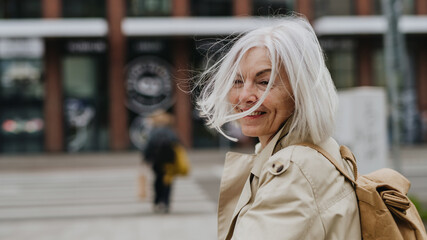 Portrait of stylish mature woman with gray hair on city street. Stunning woman crossing a road on...