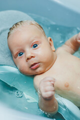 Baby hygiene. The baby lies in the bathtub and bathes. Baby bathing in water.