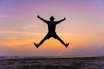 Happy young man jumping with outstretched arms on the beach with copy space. Beach silhouette...