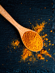 vibrant yellow turmeric spice in a rustic wooden spoon centred on a dark slate background