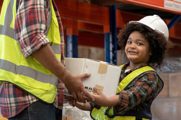 African child boy wearing a hard hat and reflective vest helps carry boxes to workers at a...