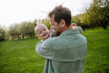 Father holding little baby, playing, having fun during warm spring day. Father's day concept.
