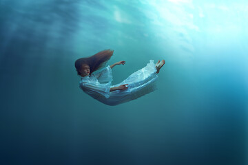 Weightlessness. Young girl with red hair, in dress gracefully falling down the ocean, showing...