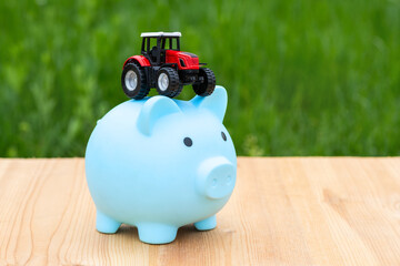 MiMiniature tractor and piggy bank on a background of grassniature tractor and piggy bank on a...