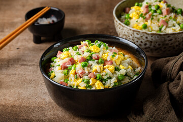 Cantonese Fried Rice with egg, green pea, ham steak, spring onion, ribe long rice in a dark bowl on...
