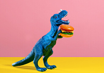 Happy blue dinosaur holding burger on pink and yellow background.