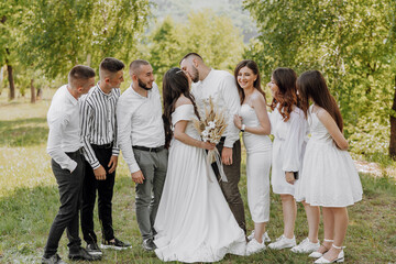 A group of people are gathered in a field, with a bride and groom in the center