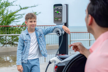 Family road trip vacation traveling by the sea with electric car, father and son recharge EV car...