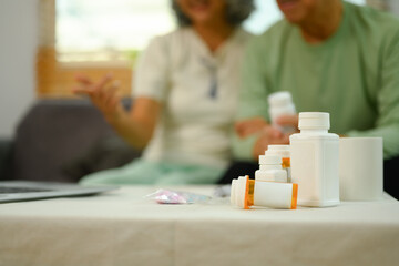 Pill bottles on table with senior couple sitting on background. Elderly healthcare, pharmaceutical concept