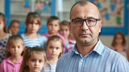 A focused male teacher stands in a classroom with young students blurred in the background, depicting education.