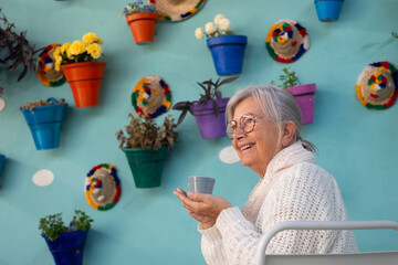 Portrait of smiling relaxed senior woman sitting at cafe table in a flowered patio enjoying pleasant moments having break with an espresso coffee cup