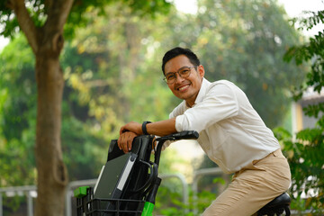 Portrait of cheerful young businessman leaning on his bicycle and smiling at camera