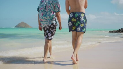 Two men in stylish beachwear leisurely stroll along the sun-kissed shore, with the tranquil blue sea beside them and the iconic twin islands in the distance. Slow motion.  - Powered by Adobe