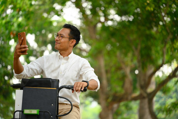 Cheerful adult asian man worker sitting on his bicycle and using mobile phone at park