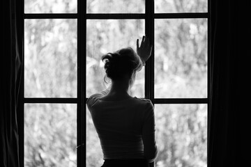 Silhouette of a woman gazing out a window, conveying solitude, longing, or contemplation, captured...