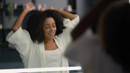 African American happy pretty woman looking mirror reflection morning biracial ethnic girl lady female at bathroom home bath stretch yawn pampering check hairdo touch face hair beauty routine wake up - Powered by Adobe