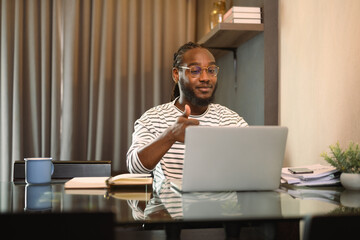 Pleased young man talking to online video call distant speaking with friends via laptop computer