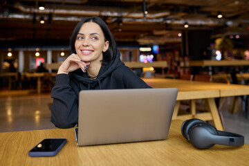 Young businesswoman spends time sitting in coffee space with laptop and headphones