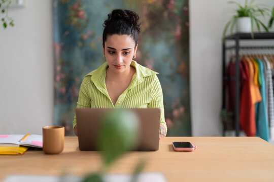 A focused South American woman in a lime-green shirt types attentively on her laptop, a glimpse into daily professional life