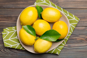 Fresh cutted lemon and whole lemons over round plate on colored background. Food and drink ingredients preparing. healthy eating theme top view vith copy space